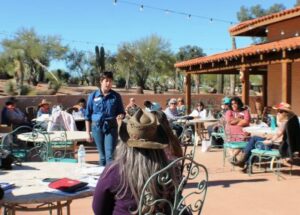 Sharon Tewksbury-Bloom facilitates a workshop outside on a patio in Wickenburg, Arizona on a sunny day. The group has a western theme.