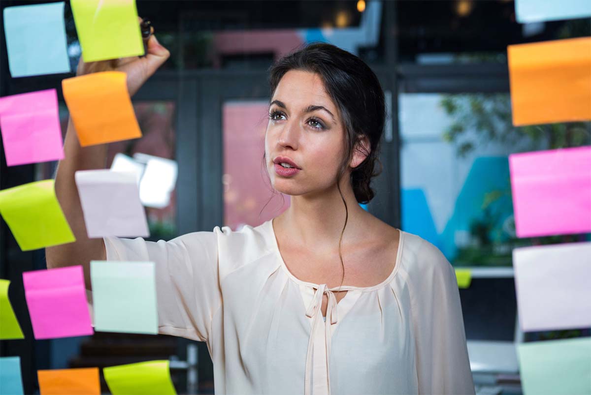 Woman Writing On Sticky Notes On Glass Wall